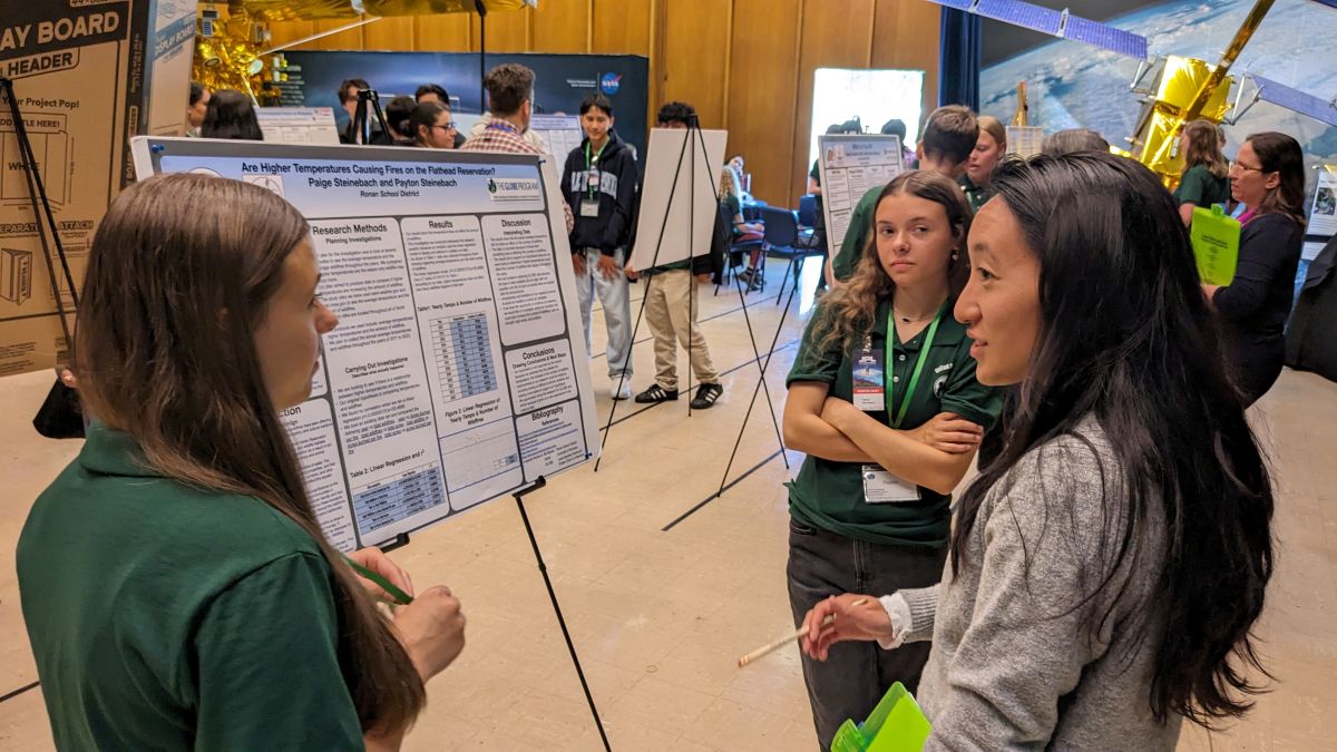 two students present their research poster to a STEM professional