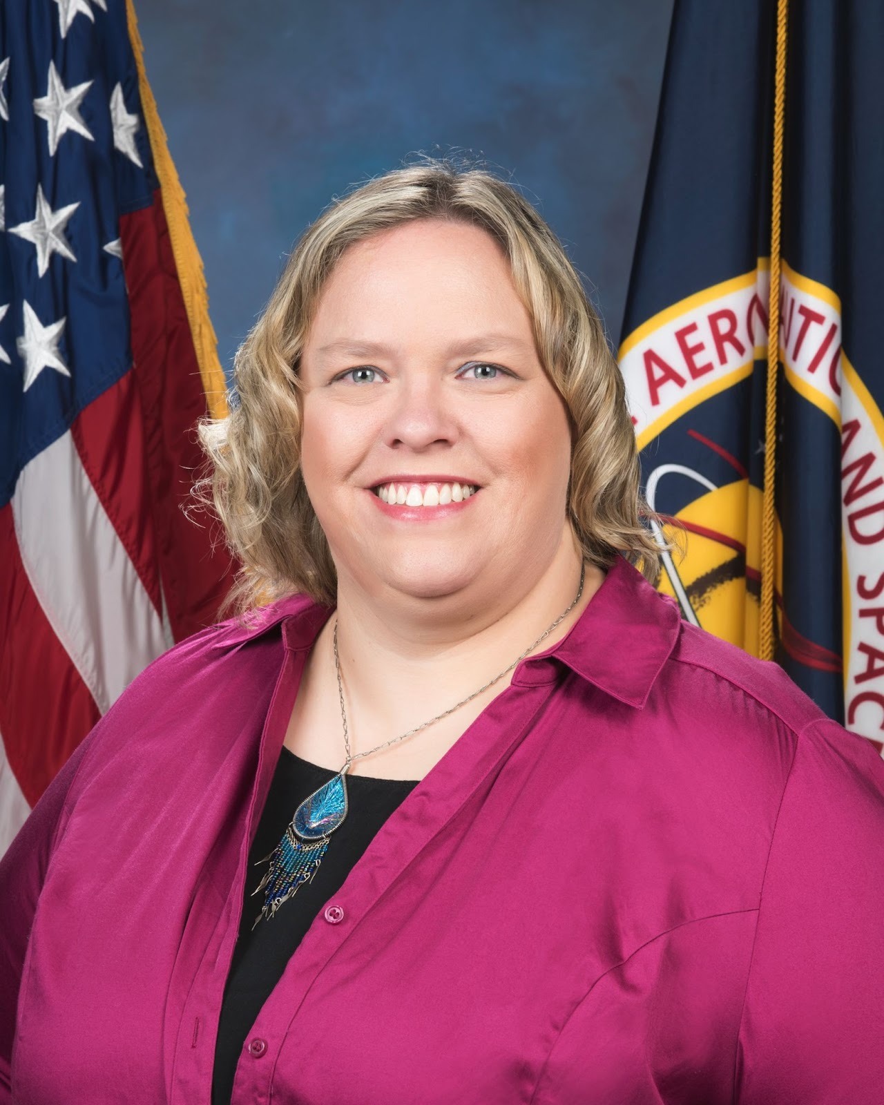 Dr. Barbie Buckner smiles brightly for a professional photo; a U.S. flag and a NASA flag are behind her.